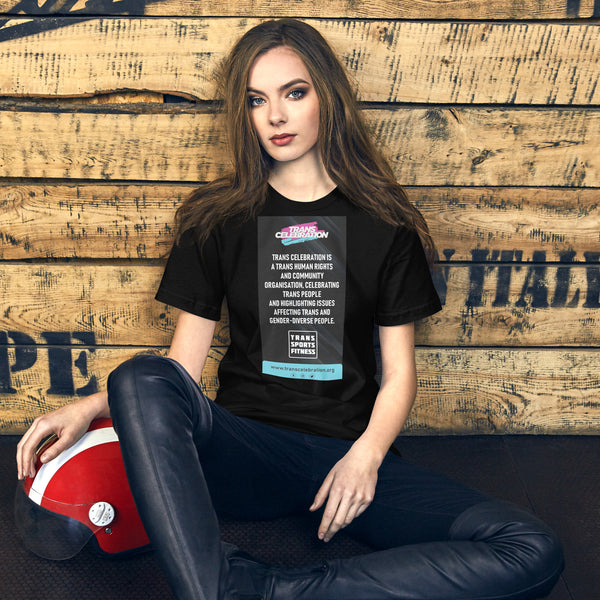 Model in black "Trans Celebration" message t-shirt, seated against a wooden backdrop with a red helmet by her side, promoting trans rights awareness
